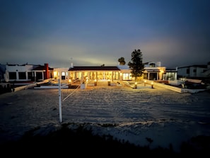 A beachfront property with a well-lit building, outdoor seating, and a sandy beach area.
