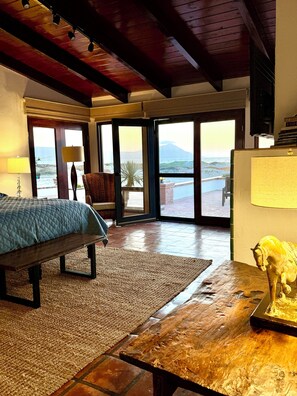 A room with a bed, a rug, a table with a sculpture, and a view of the outdoors through large glass doors.
