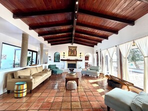 A spacious living area with a high wooden ceiling, large windows, and a fireplace.