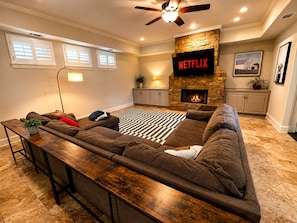 Ein Wohnzimmer mit einer großzügigen Eckcouch, einem Holztisch, einem Kamin und einem an der Wand montierten Fernseher, der 'NETFLIX' zeigt.