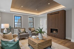 A modern living room with a fireplace, two sofas, a coffee table, and a large window. - Modern Luxury Commercial St Condo • 3 En-Suite BRs (Provincetown)