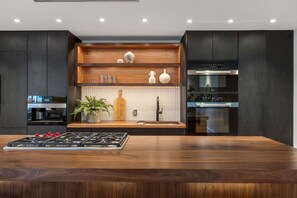 A modern kitchen with a central island, built-in appliances, and wooden shelving. - Modern Luxury Commercial St Condo • 3 En-Suite BRs (Provincetown)