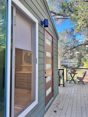 Une maison dotée d’une porte-fenêtre coulissante donnant sur un intérieur en bois, d’une petite terrasse extérieure avec une table et une chaise, et d’une plante en pot.