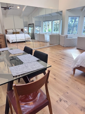A modern hotel room with a glass dining table, a wooden chair, a bed, and a large mirror reflecting the room. - Newly Remodeled Luxe Canyon Studio Hideaway (San Diego)