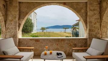 Une pièce aux murs de pierre, avec vue sur un plan d’eau et des montagnes. On y trouve deux canapés et une petite table sur laquelle sont posés un verre de jus d’orange et un téléphone intelligent.