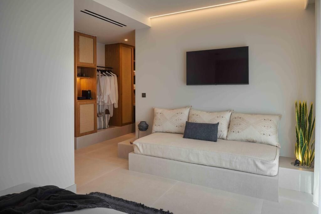 Un dormitorio moderno con sofá cama, televisor montado en la pared y vestidor.