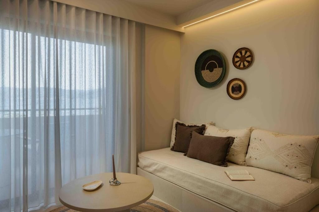 Una habitación con sofá, una mesa redonda y una ventana con cortinas de gasa.