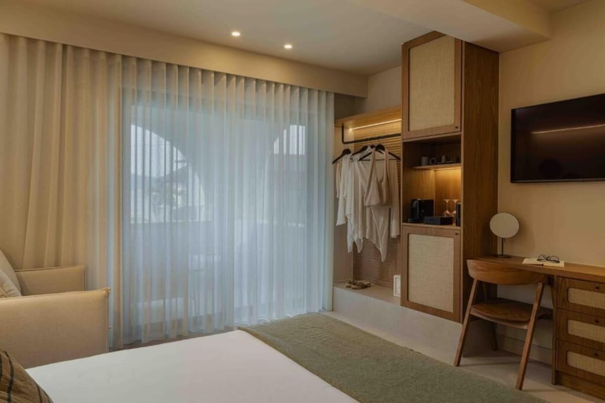 Quarto de hotel com cama, escrivaninha, cadeira, televisão e guarda-roupa.
