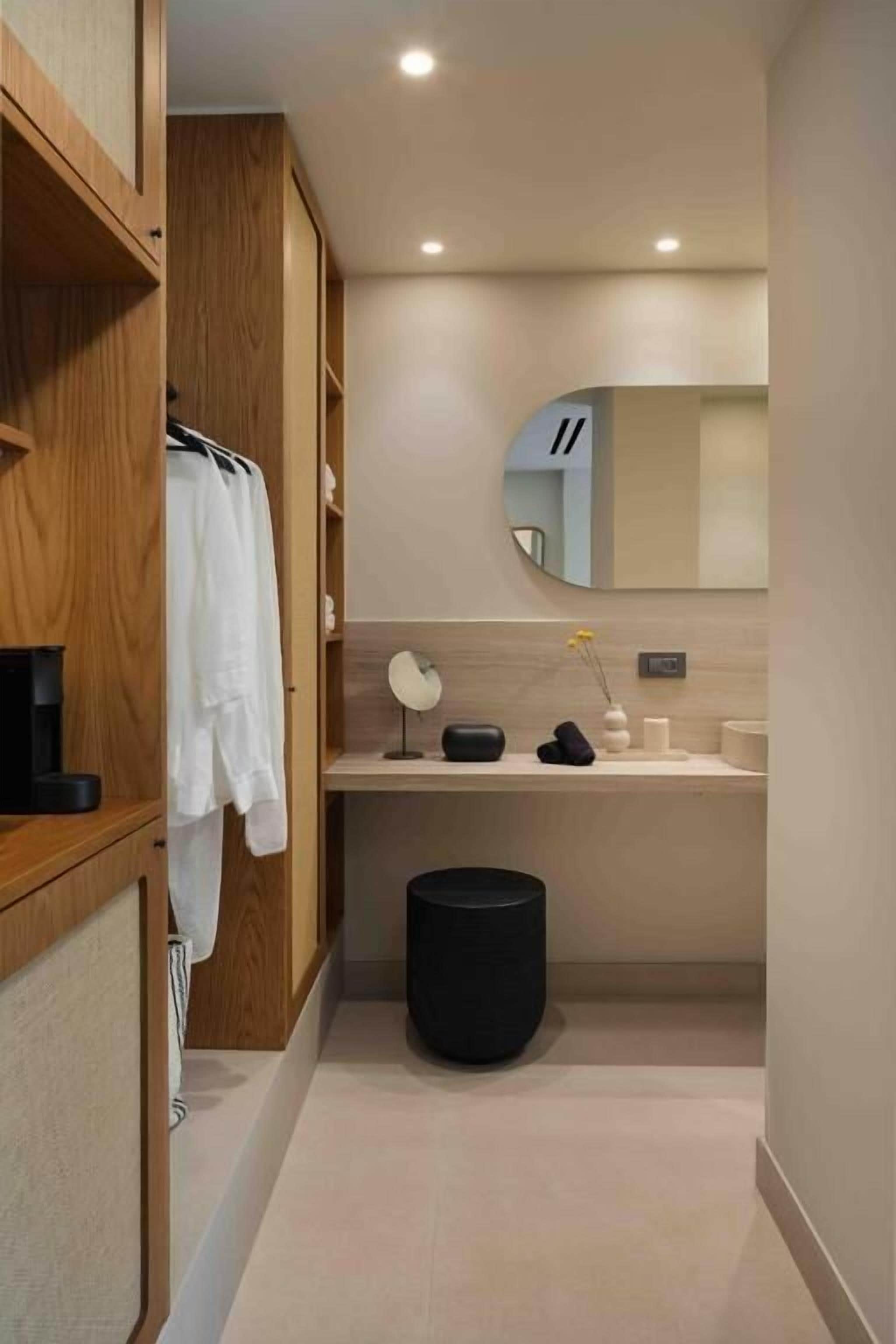 Une salle de bain moderne avec des meubles en bois, un miroir rond, un lavabo et une poubelle noire.