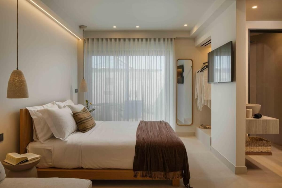 Quarto moderno com cama, mesa de cabeceira e um espelho grande.