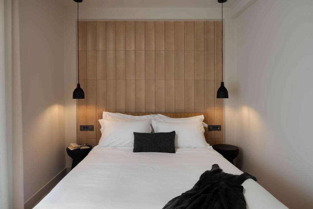 Quarto de hotel com uma cama grande, duas mesas de cabeceira e uma cabeceira fixada na parede.