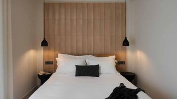 Quarto de hotel com uma cama grande, duas mesas de cabeceira e uma cabeceira fixada na parede.