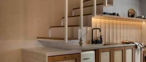 A modern kitchen with a built-in dishwasher, wooden cabinetry, and a staircase leading to an upper level.
