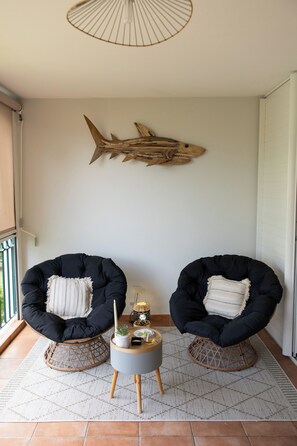 Une pièce comprenant deux fauteuils noirs rembourrés, une petite table ronde avec une bougie et une plante, et une décoration murale en forme de requin en bois.