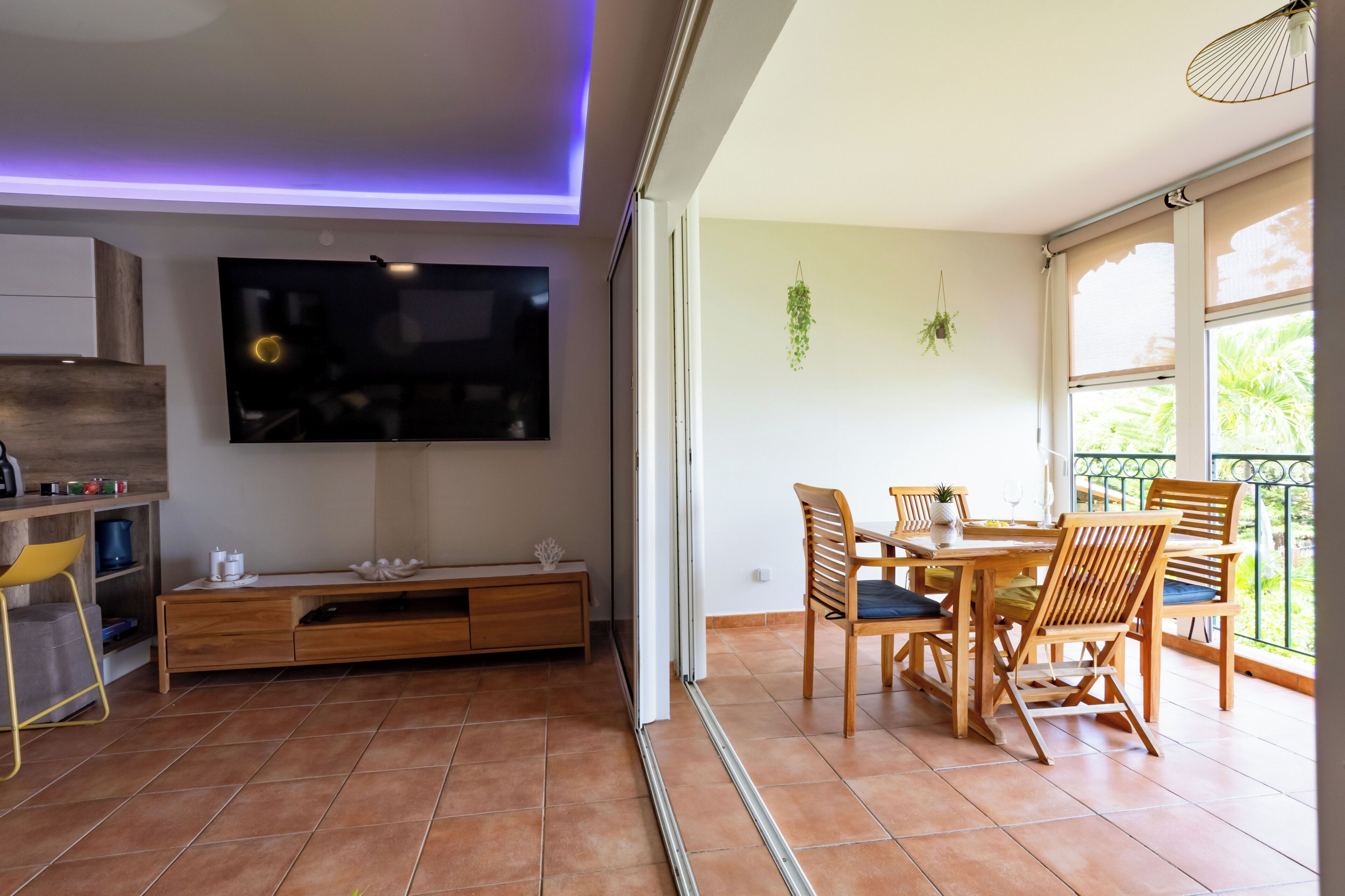 A modern living room with a flat-screen TV, wooden furniture, and a balcony with a view.