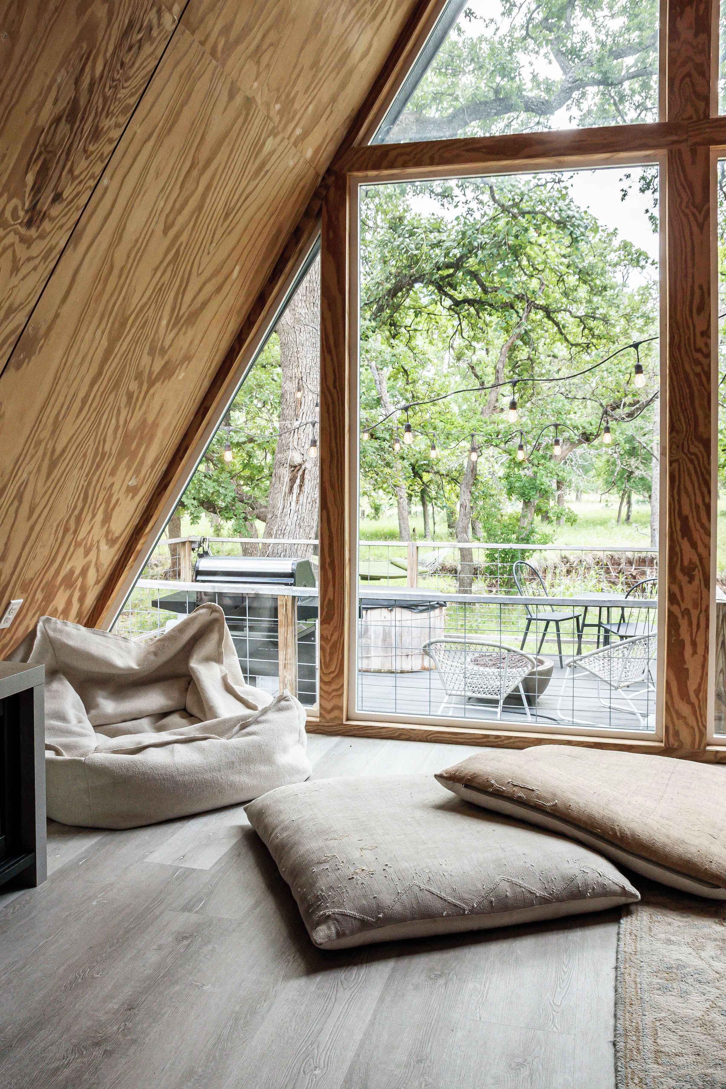 Une pièce avec un plafond en pente, une grande fenêtre et une vue sur les arbres et un espace patio.