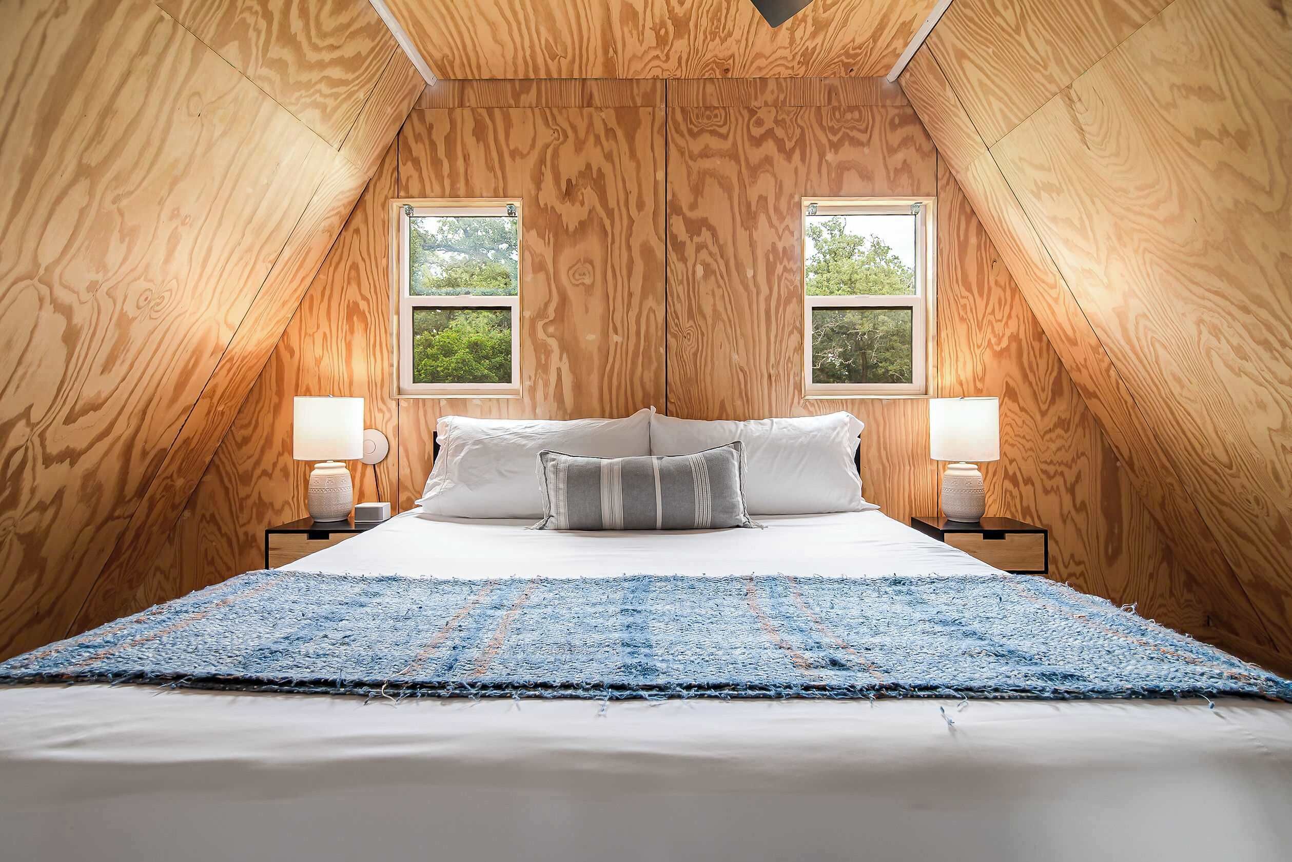 Une chambre avec un plafond en pente, deux fenêtres, un lit avec des oreillers et des lampes de chevet.