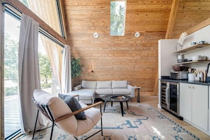 A cozy interior with a sofa, a chair, a coffee table, and a kitchen area with cabinets and a countertop. - A-Frame Ranch: Post Oak Treehouse with Shared Pool (Fredericksburg)