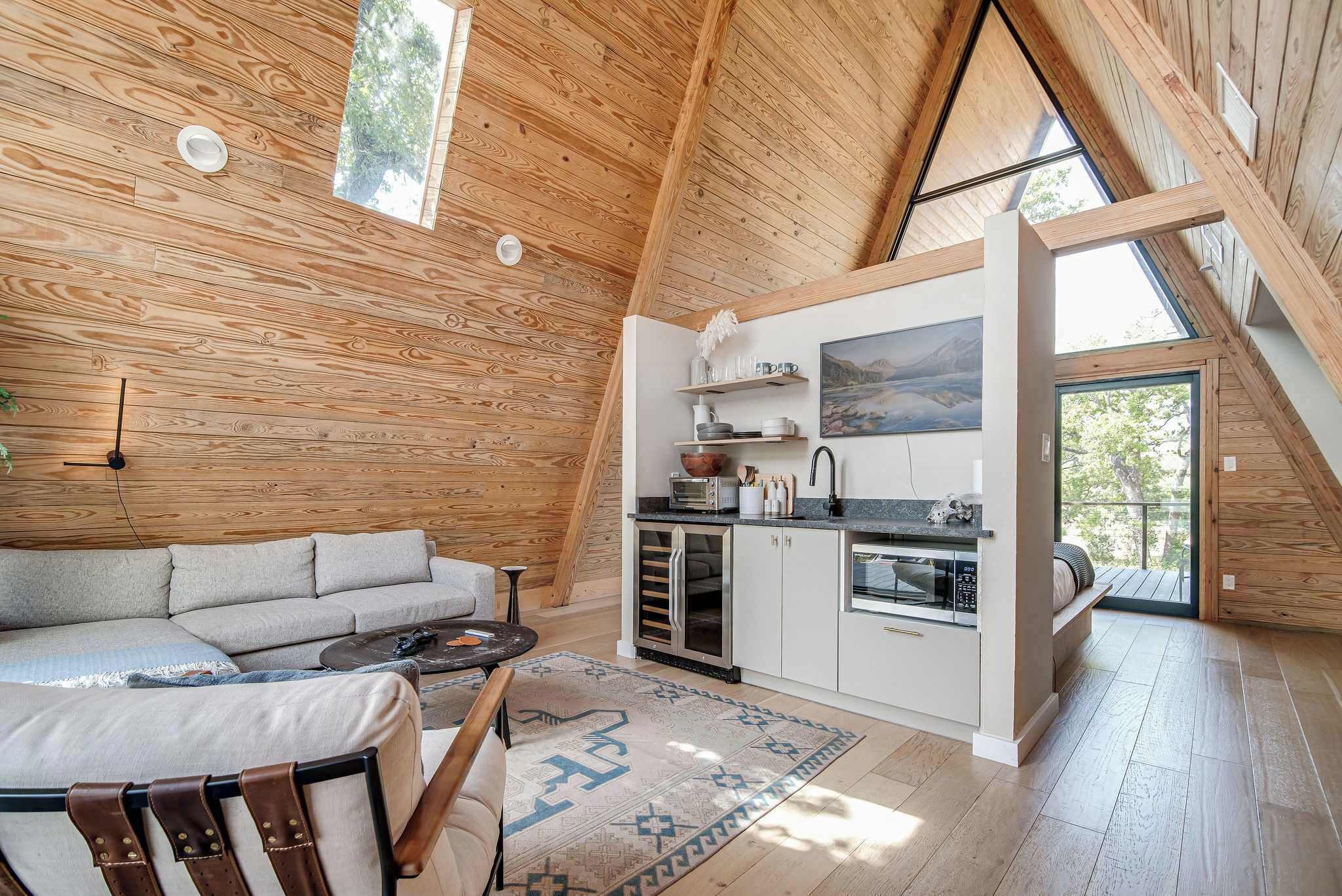Un espace de vie chaleureux de style loft, avec un intérieur en bois, un canapé, une table basse et un coin cuisine équipé d’appareils électroménagers.