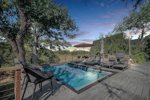 A swimming pool with lounge chairs and a barbecue area, surrounded by trees and a wooden deck. - A-Frame Ranch: Post Oak Treehouse with Shared Pool (Fredericksburg)
