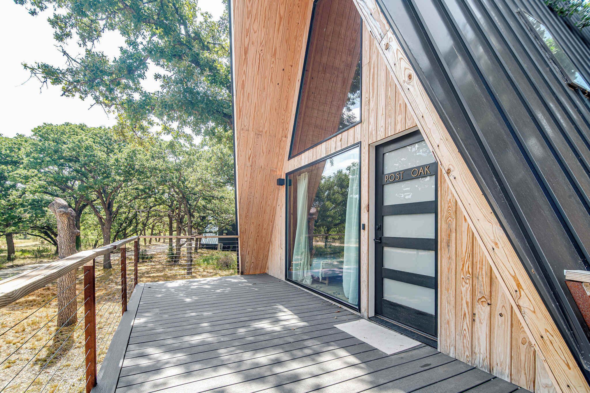 Un bâtiment moderne en bois, doté d’une porte en verre portant l’inscription « POST OAK » et d’une terrasse en bois.