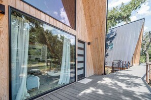 A modern building with large glass windows, a wooden deck, and a metal railing. - A-Frame Ranch: Post Oak Treehouse with Shared Pool (Fredericksburg)