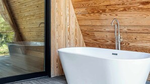 A modern bathroom with a freestanding bathtub, wooden slatted ceiling, and a large window. - A-Frame Ranch: Post Oak Treehouse with Shared Pool (Fredericksburg)