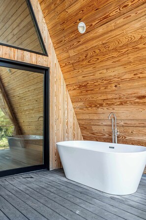 Ein modernes Badezimmer mit einer freistehenden Badewanne, einer Holzboden-Decke und einem großen Fenster.