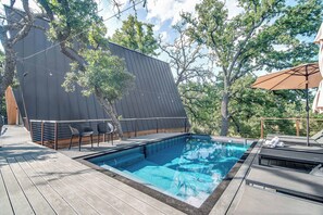 A swimming pool with a deck, lounge chairs, and a large umbrella. - A-Frame Ranch: Post Oak Treehouse with Shared Pool (Fredericksburg)