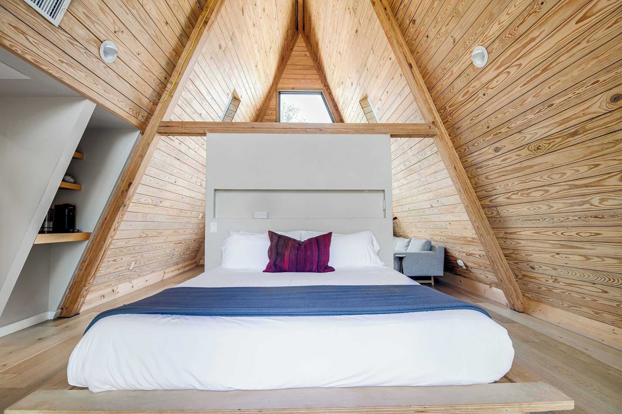 Une chambre avec un plafond en pente, un lit avec une literie blanche, un oreiller rouge et une table de chevet avec une lampe.