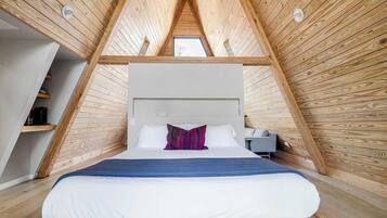 Une chambre avec un plafond en pente, un lit avec une literie blanche, un oreiller rouge et une table de chevet avec une lampe.