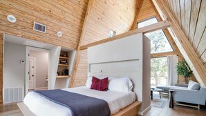 A modern bedroom with a large bed, a built-in bench, a bedside table, and a view of the outdoors through a skylight. - A-Frame Ranch: Post Oak Treehouse with Shared Pool (Fredericksburg)