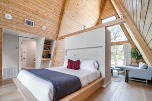 Ein modernes Schlafzimmer mit einem großen Bett, einer eingebauten Sitzbank, einem Nachttisch und Blick ins Freie durch ein Oberlicht.