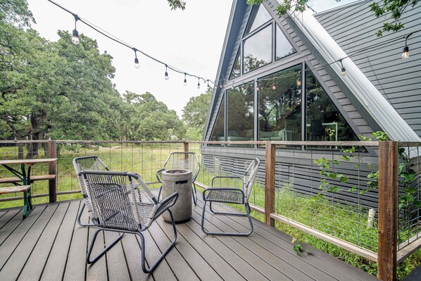 Eine Terrasse mit zwei Metallstühlen und einem Tisch, mit Blick auf eine Rasenfläche und ein Haus mit großen Fenstern.