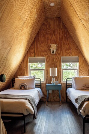 A cozy attic bedroom with two beds, a small table, and a wall-mounted skull decoration. - A-Frame Ranch: Llano Cabin with Cowboy Pool (Fredericksburg)