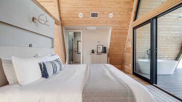 A modern bedroom with a large bed, a wooden ceiling, and a sliding glass door leading to a bathroom with a bathtub.