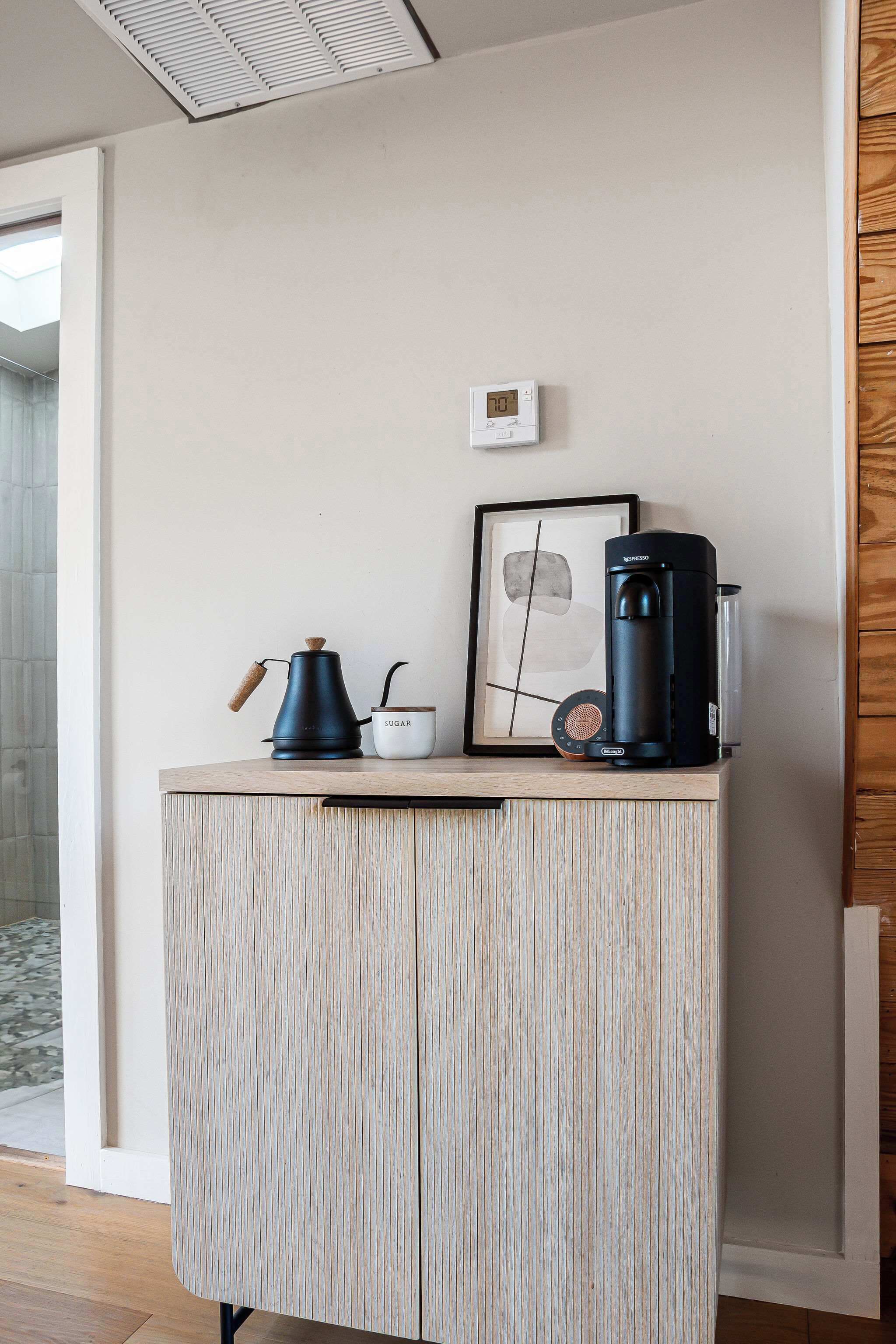 A kitchenette with a coffee maker, a kettle, and a framed picture on a wooden cabinet.