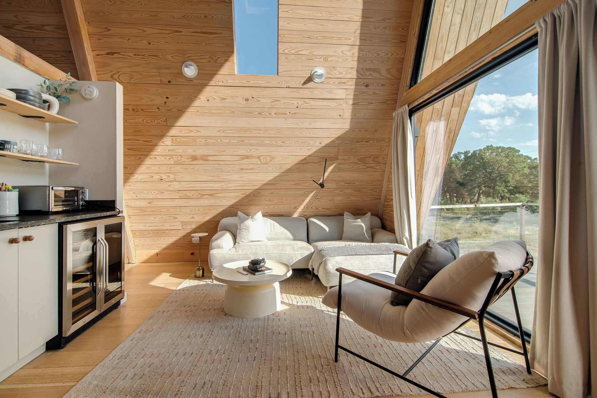 Un salon moderne avec un canapé, une table basse et un fauteuil, un plafond en bois et de grandes fenêtres.