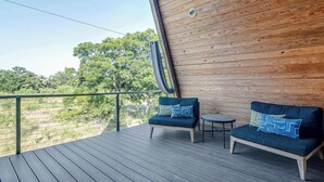 A wooden deck with two dark blue sofas and a small round table, overlooking a green landscape. - A-Frame Ranch: Cedar Treehouse with Shared Pool (Fredericksburg)