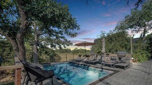 A swimming pool with lounge chairs and a barbecue area, surrounded by trees and a wooden deck. - A-Frame Ranch: Cedar Treehouse with Shared Pool (Fredericksburg)
