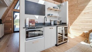 A compact kitchen with a built-in oven, microwave, and dishwasher, wooden ceiling beams, and a large window. - A-Frame Ranch: Cedar Treehouse with Shared Pool (Fredericksburg)