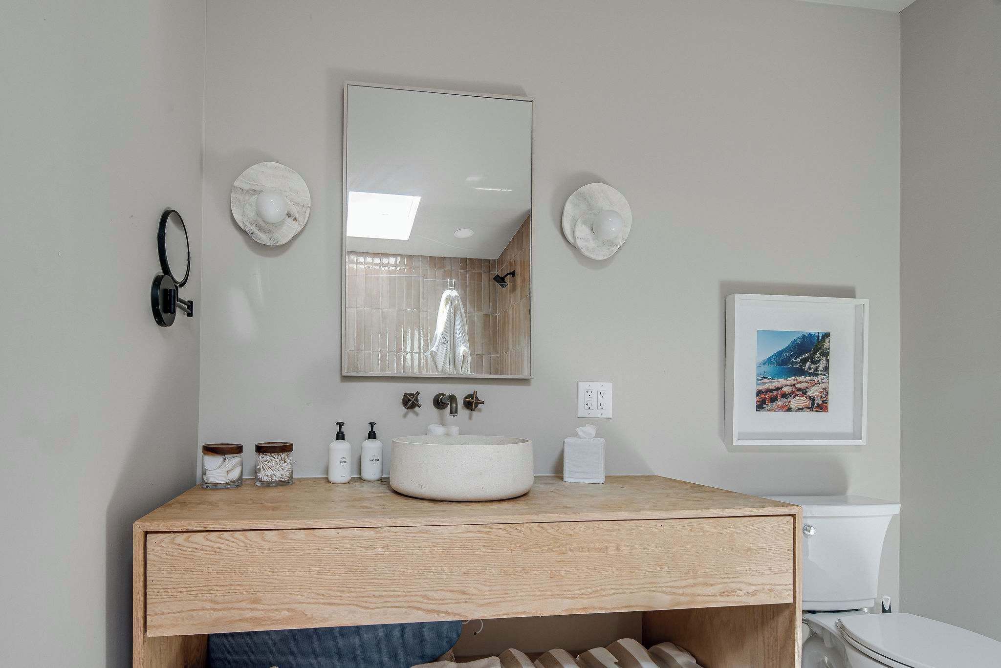 A bathroom with a wooden vanity, a round sink, a mirror, and a framed picture on the wall.