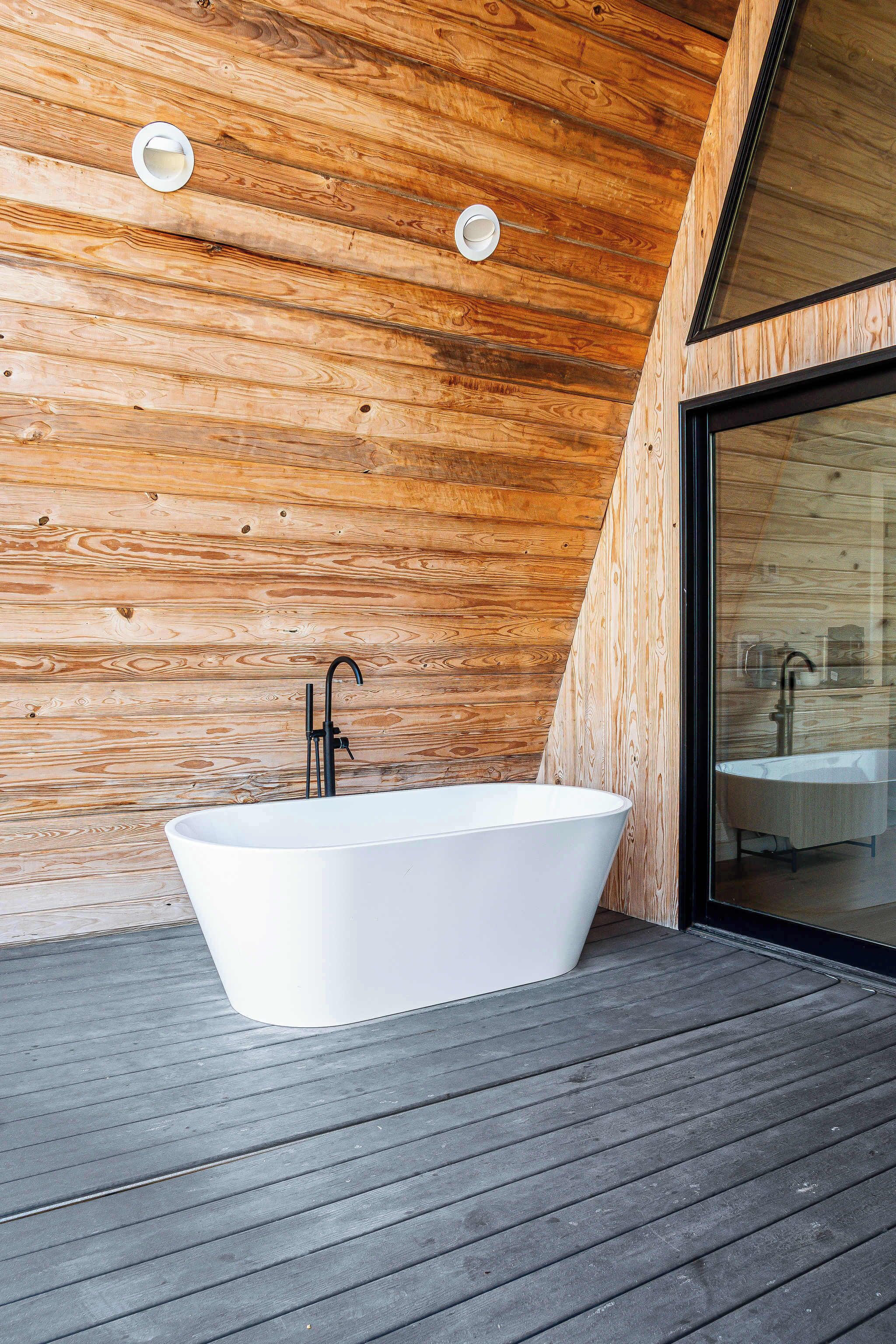 A modern bathroom with a freestanding bathtub, wooden wall paneling, and a glass shower enclosure.