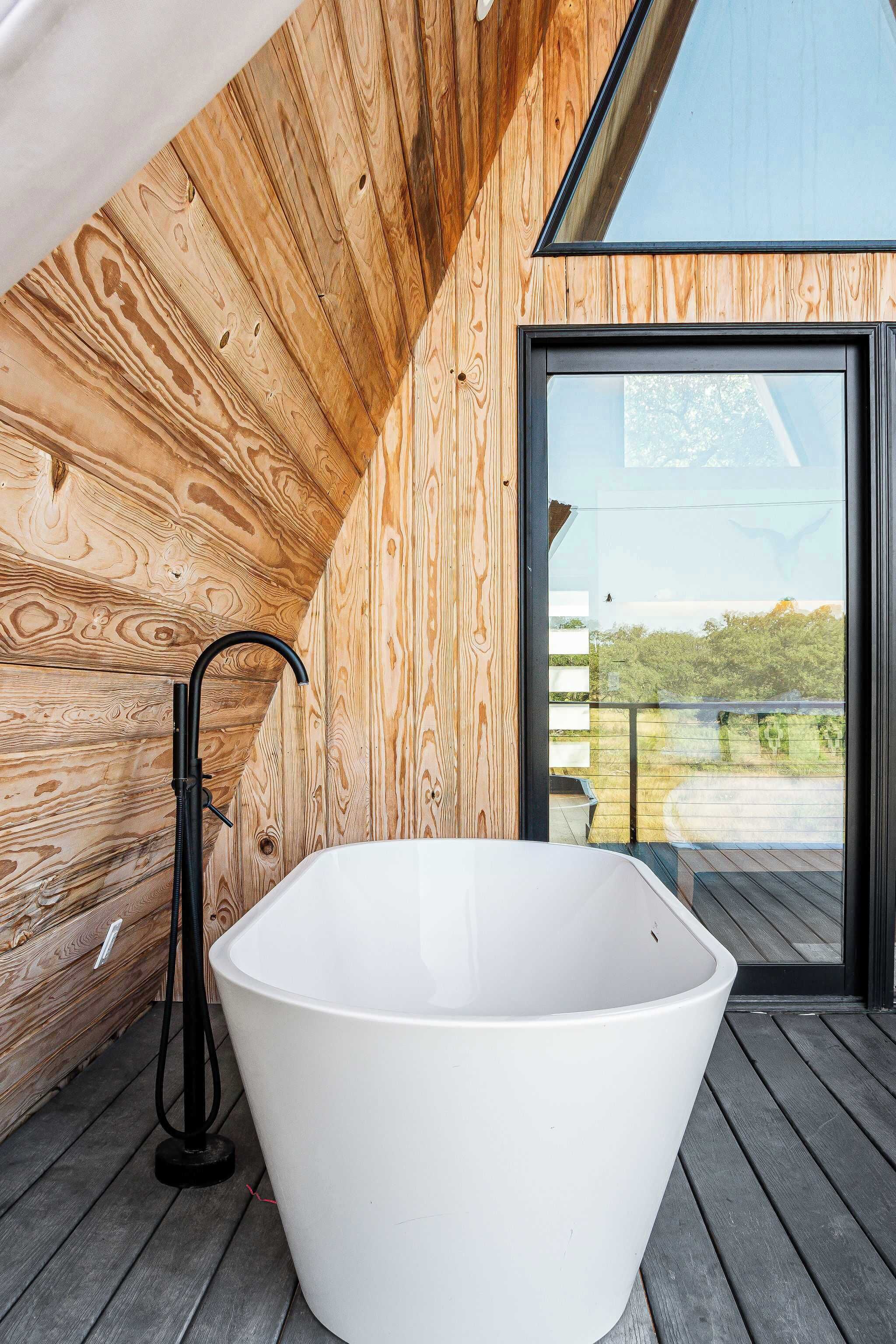 A modern wooden interior with a freestanding bathtub and a large window offering a view of the outdoors.