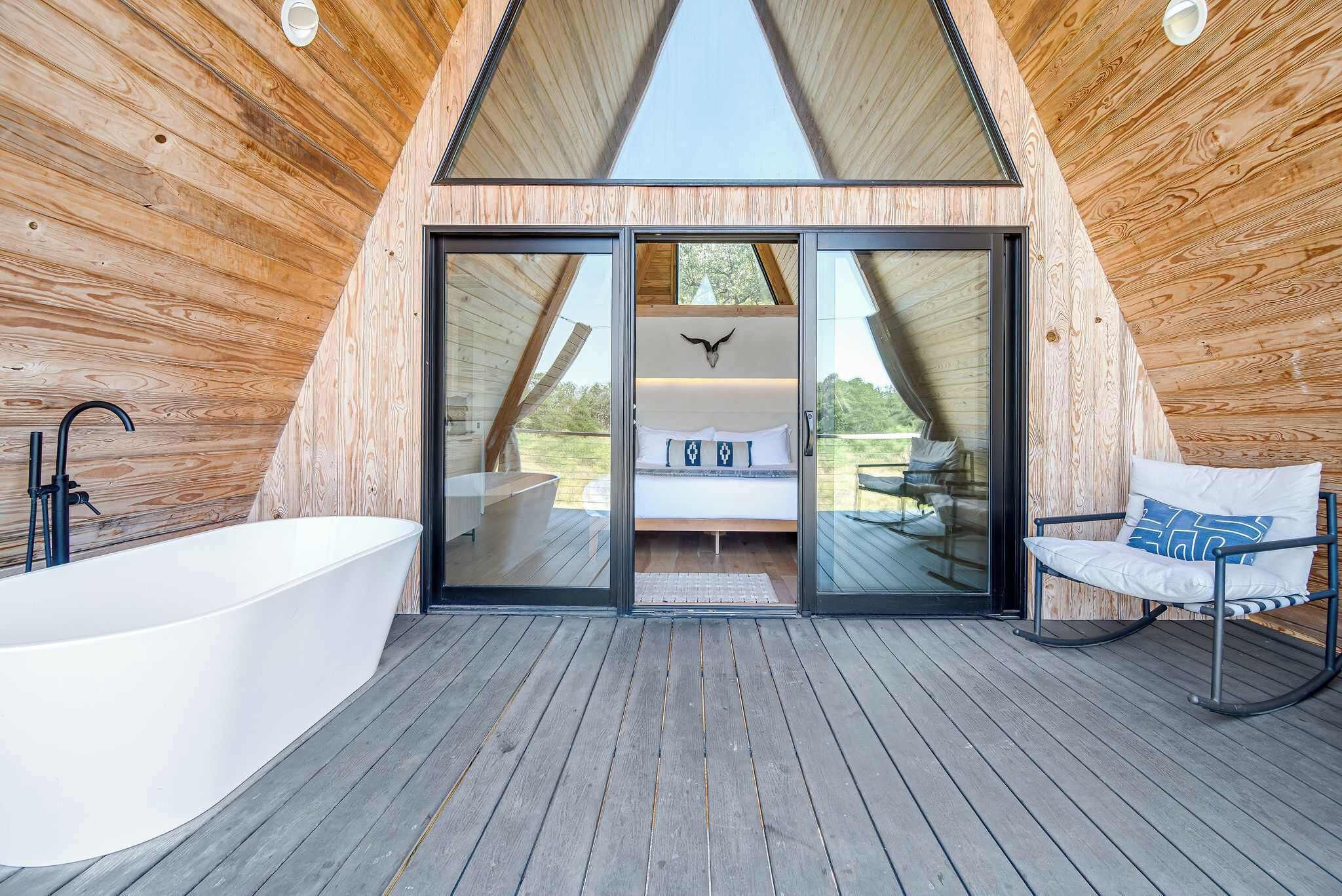 Ein modernes Interieur aus Holz mit einer großen Badewanne, einem Bett mit Blick und einem Schaukelstuhl.