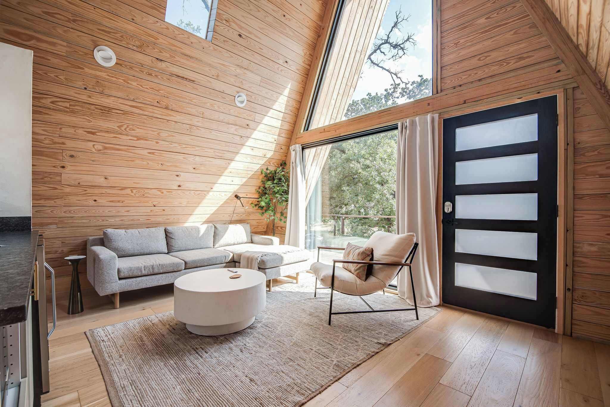 A modern interior with a wooden sloped ceiling, a sofa set, a round coffee table, and a large sliding glass door.
