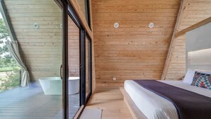 A modern bedroom with a large bed, a view of the outdoors, and a wooden ceiling. - A-Frame Ranch: Pecan Treehouse with Shared Pool (Fredericksburg)