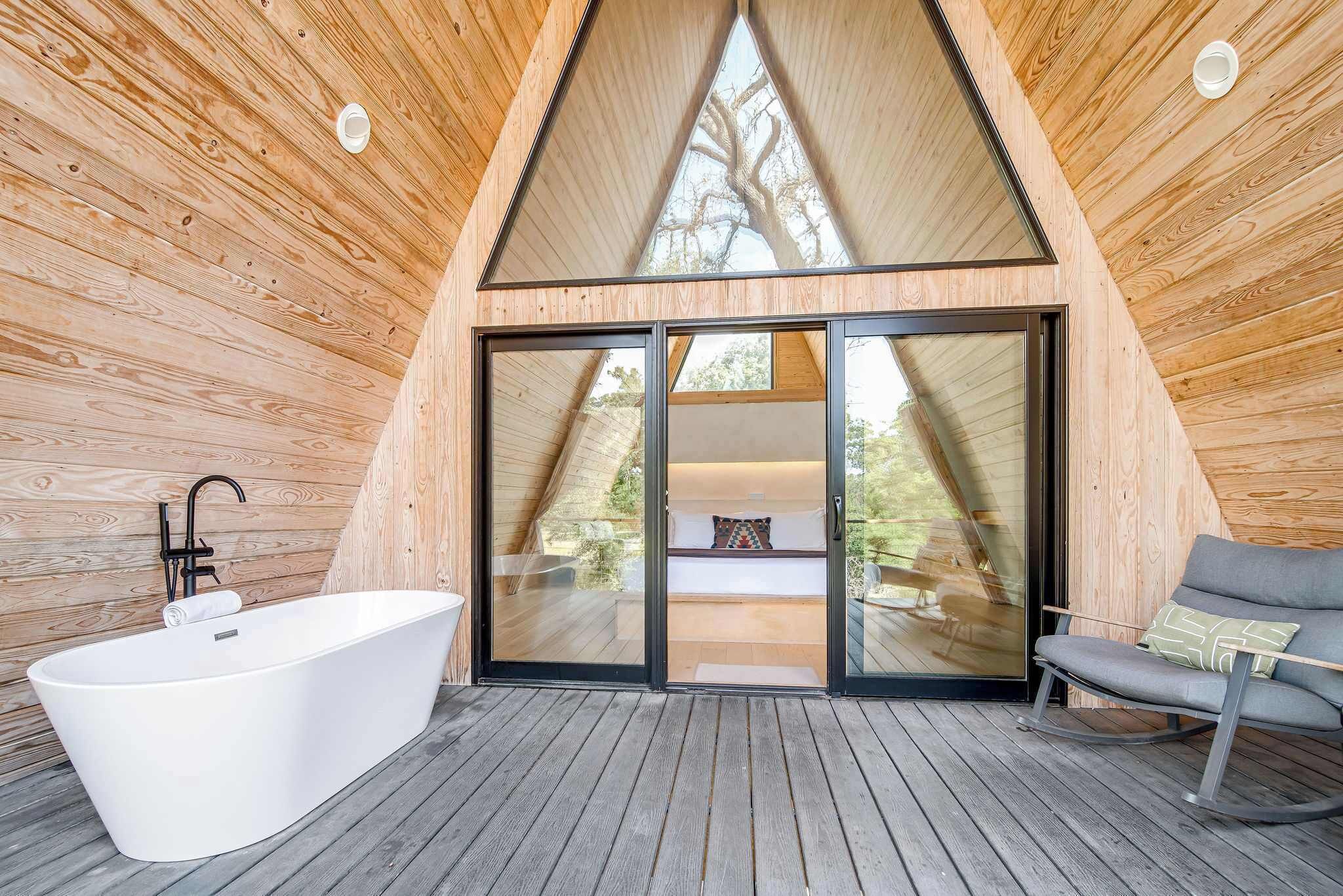 A modern, wooden interior with a large bathtub, a seating area, and a glass door leading to an outdoor space.