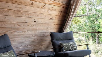 Eine Holzterrasse mit zwei Schaukelstühlen und einem kleinen Tisch, mit Blick auf eine natürliche Landschaft.