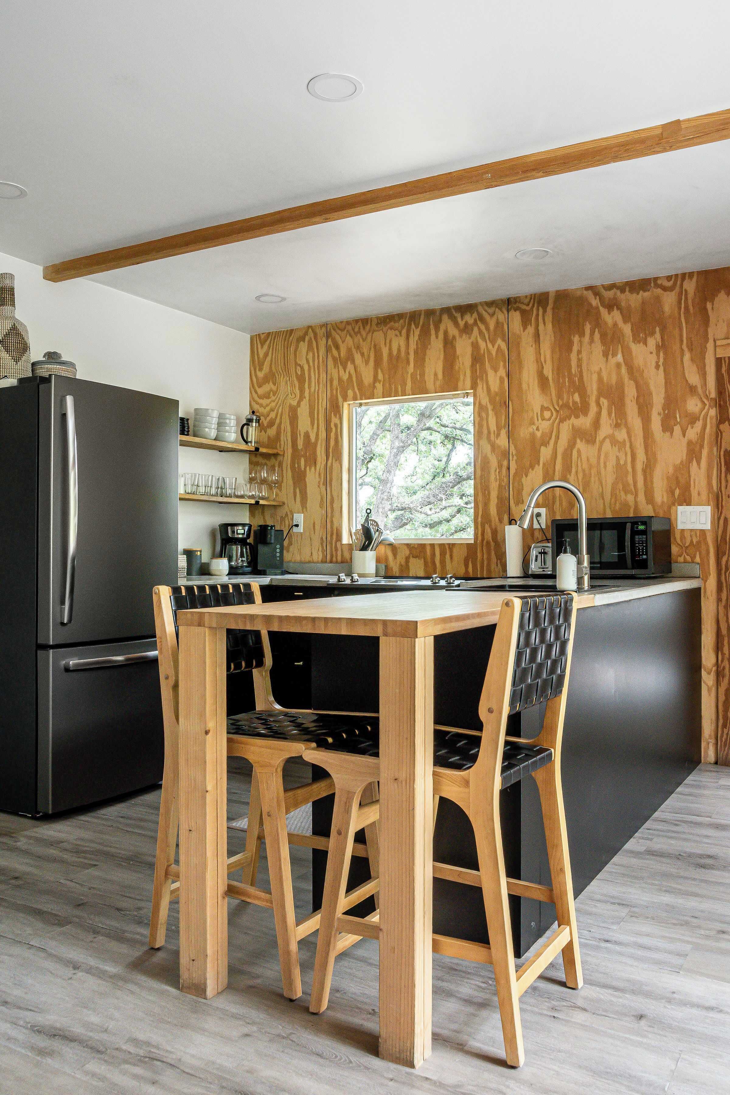 A modern kitchen with a wooden island, black appliances, and a view of trees through a window.